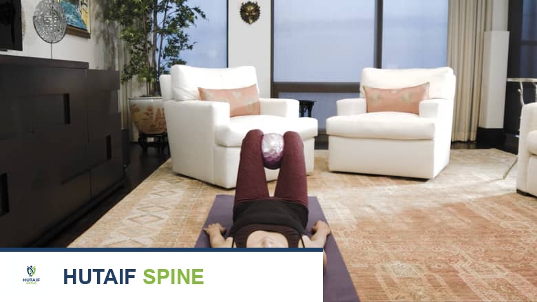 امرأة تؤدي تمرين ضم الورك أثناء الاستلقاء باستخدام كرة طبية على سجادة اليوغا.